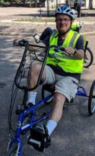 An Elderhaus participant in a bike helmet and safety vest riding a recumbent trike